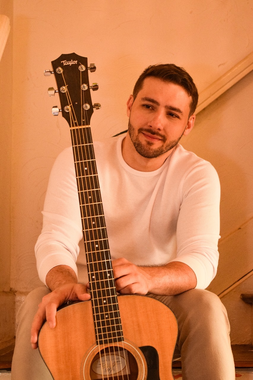 Roger Loeblein sentado na escada segurando o violão