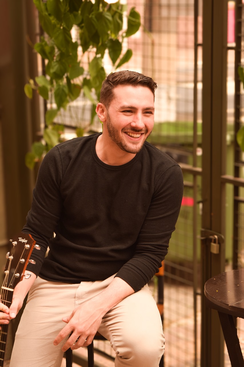 Roger Loeblein sorrindo ao ar livre com o violão na mão