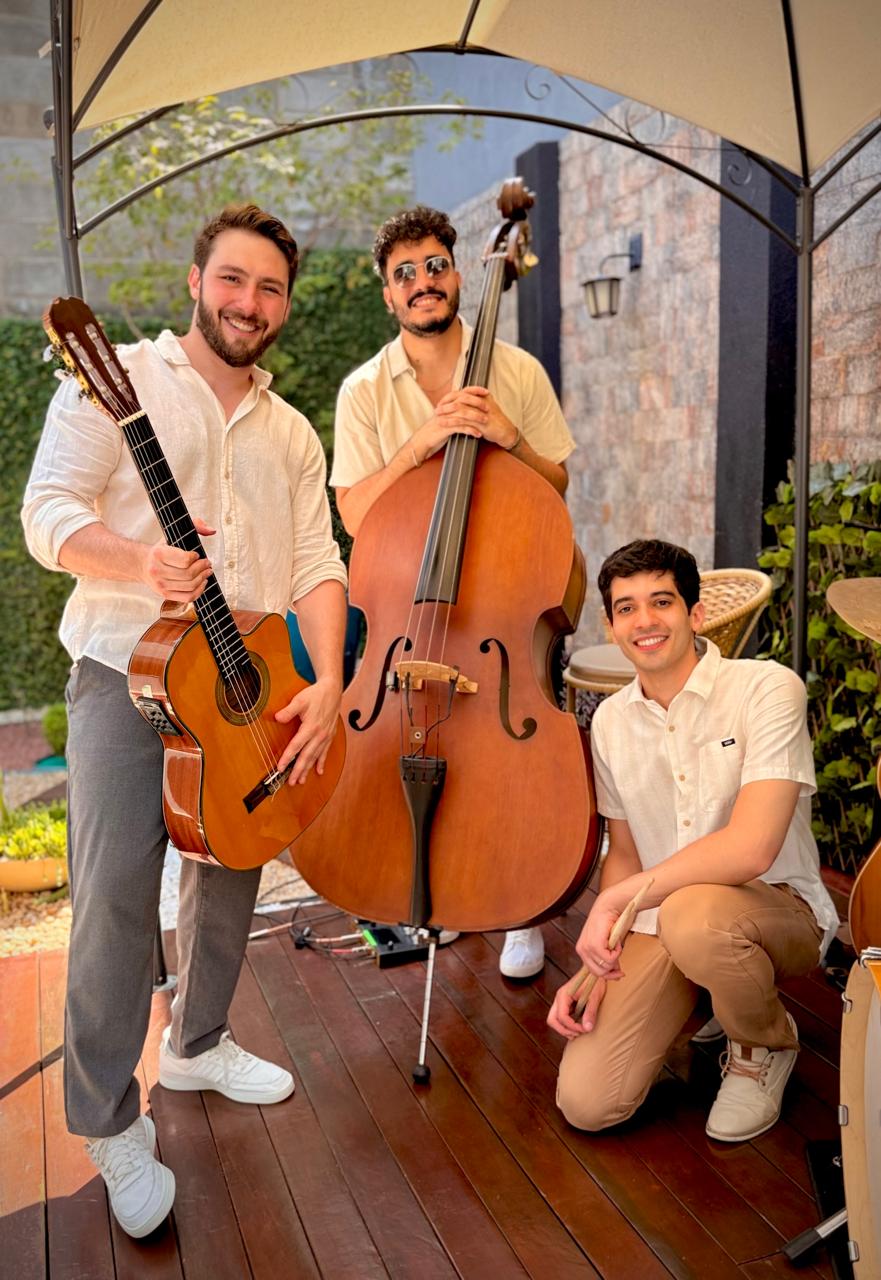 Trio musical com violão, contrabaixo acústico e percussão sob uma tenda