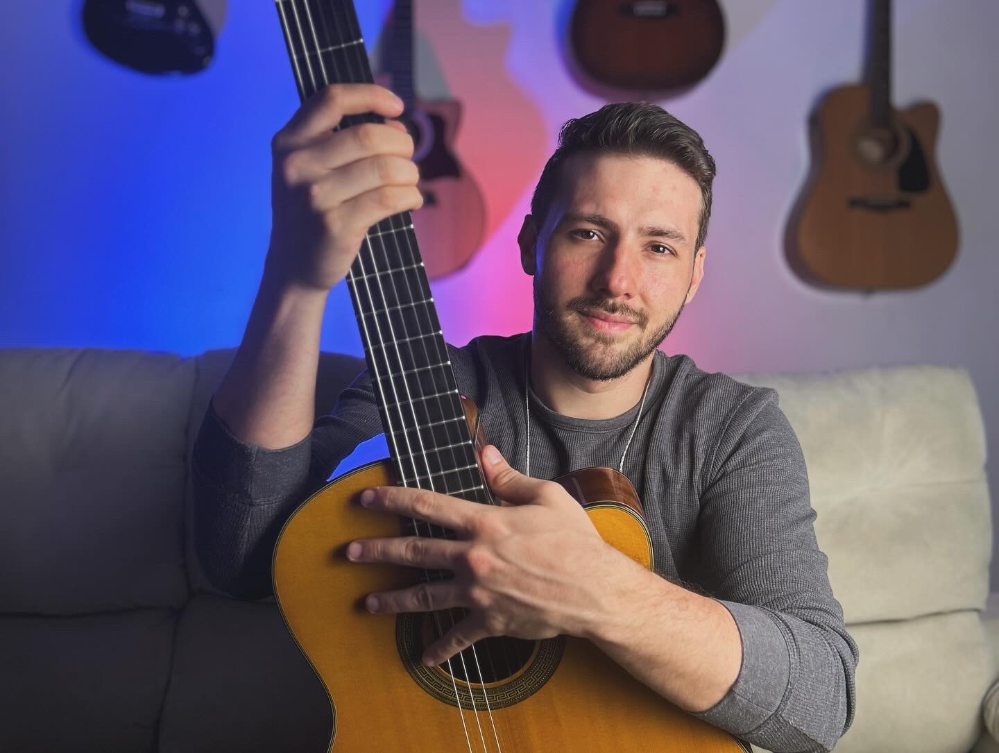 Roger Loeblein com um violão de nylon em um estúdio caseiro, com luzes coloridas ao fundo
