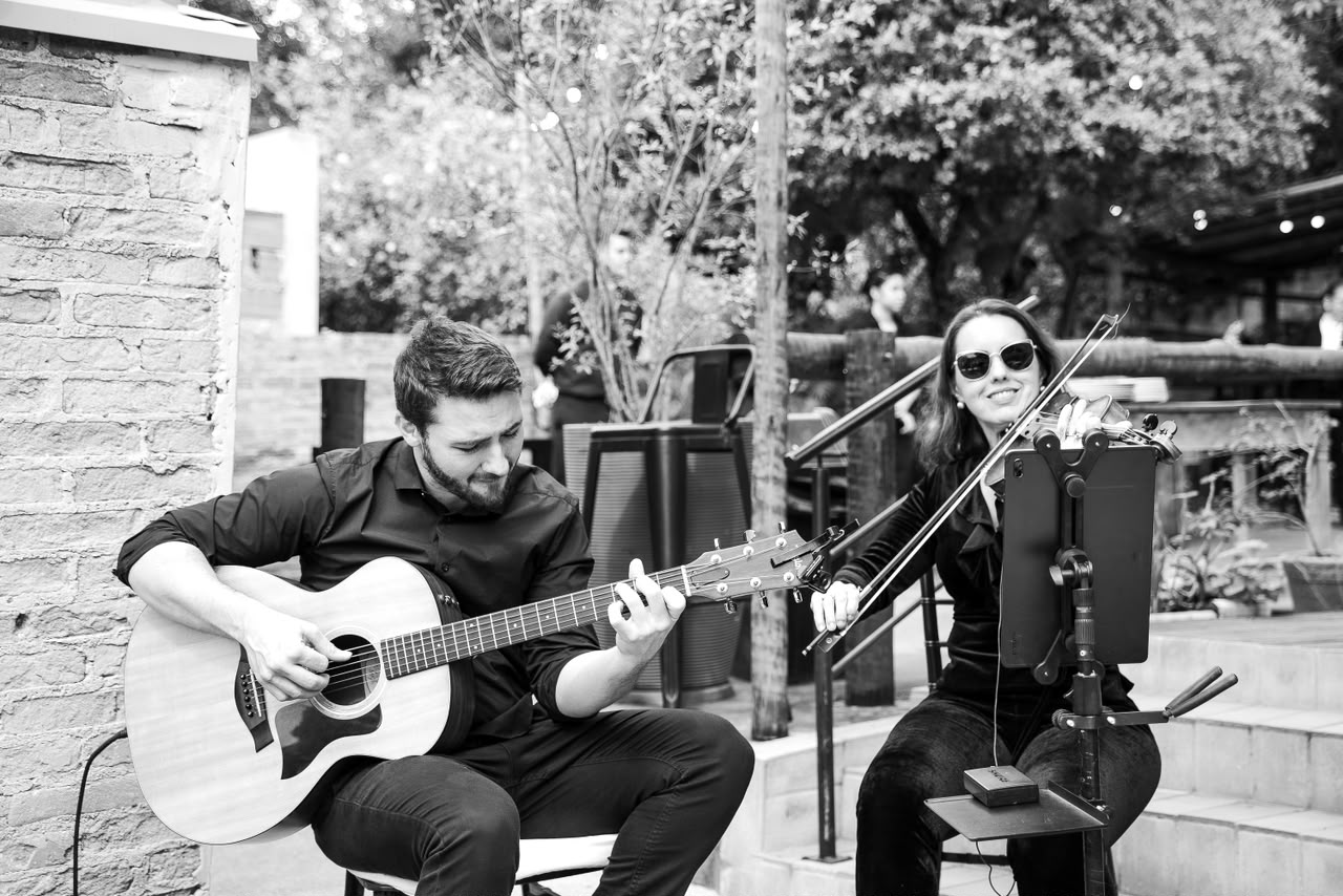 Roger Loeblein ao violão e uma violinista tocando em um evento ao ar livre